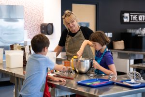 Two children and a cooking instructor working in a kitchen.