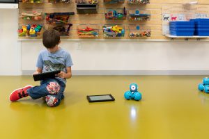 Child sitting on floor with tablet next to robot.