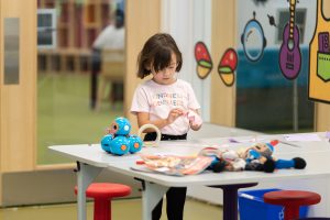 Child working at a craft table holding a paper crown.